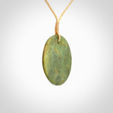 This piece is a medium sized, oval round, disc pendant. It is suspended on a beige coloured braided cord that is length adjustable.